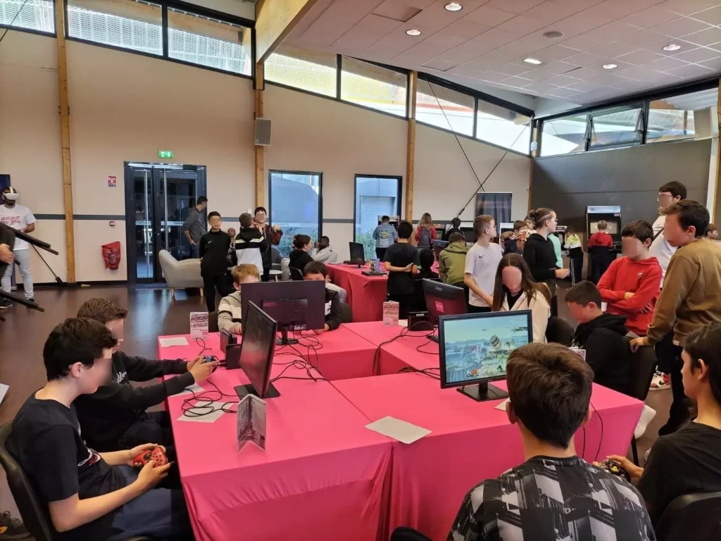 Plan d'ensemble du lieu. Au prmier plan des enfants qui jouent à des jeux vidéo