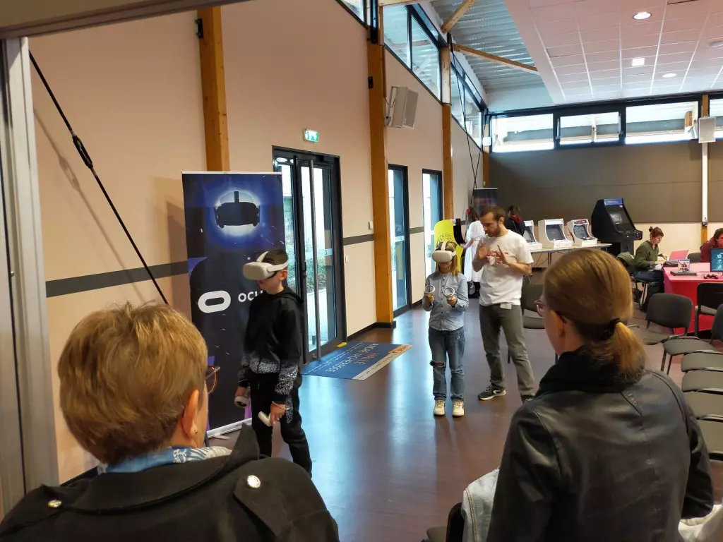 Espace réalité virtuelle, deux enfants munis de casques VR, un animateur, des parents qui regardent